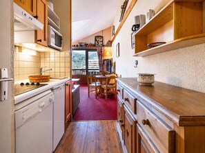 A compact kitchen with wooden cabinets, a microwave, and a red rug leading to a dining area. - Cozy studio cabin with wifi and parking in Val-d'Isère (Val-d'Isère)