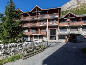 A multi-story wooden building with balconies, stone walls, and a sign indicating it is a ski resort.