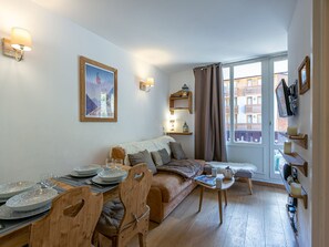Un salon chaleureux avec un coin repas, des meubles en bois, un canapé, une table avec des assiettes et des verres, un tableau encadré et un téléviseur fixé au mur.