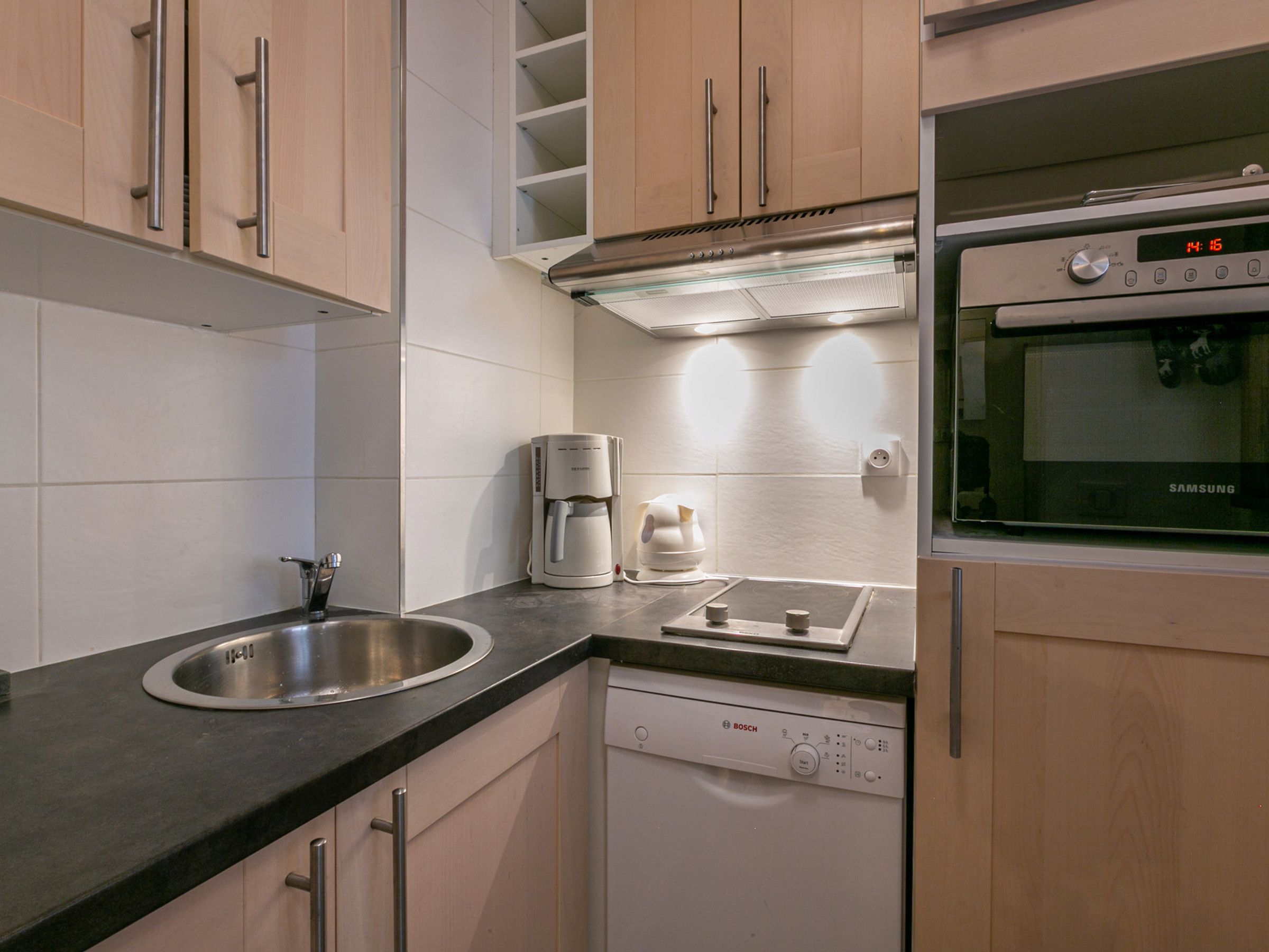 A modern kitchen with a stainless steel sink, a coffee maker, a Bosch dishwasher, and a Samsung oven.