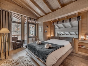 A bedroom with a large bed, a chair, a desk, and a window with curtains. - Luxury Duplex Apartment in Central Val-d'Isère, Near Slopes, with Large South-Facing Terrace (Val-d'Isère)