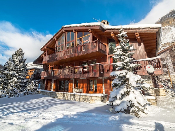 A multi-story wooden chalet with balconies, surrounded by snow-covered trees and a clear blue sky. - Luxury Duplex Apartment in Central Val-d'Isère, Near Slopes, with Large South-Facing Terrace (Val-d'Isère)