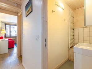 A hallway with a wooden floor, a red chair, a white cabinet, and a window with curtains.