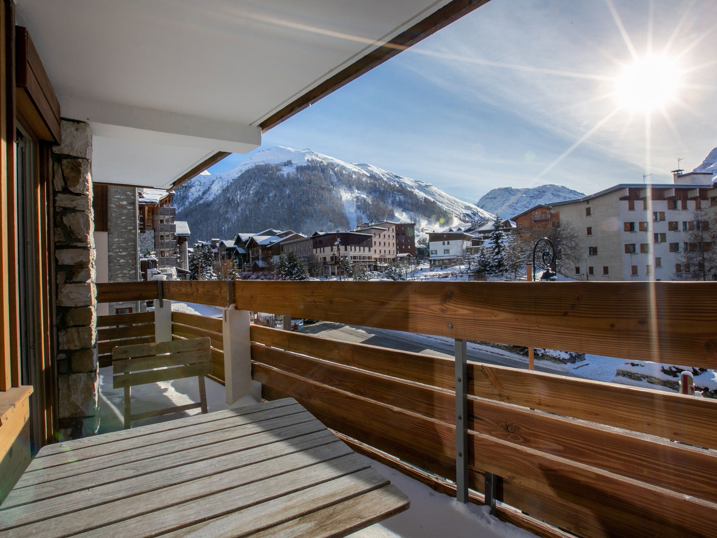 A wooden deck with a view of a snow-covered mountain and buildings.