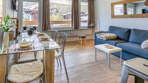 Una sala moderna con una mesa de comedor de vidrio, un sofá azul y vistas a un pueblo a través de amplios ventanales.