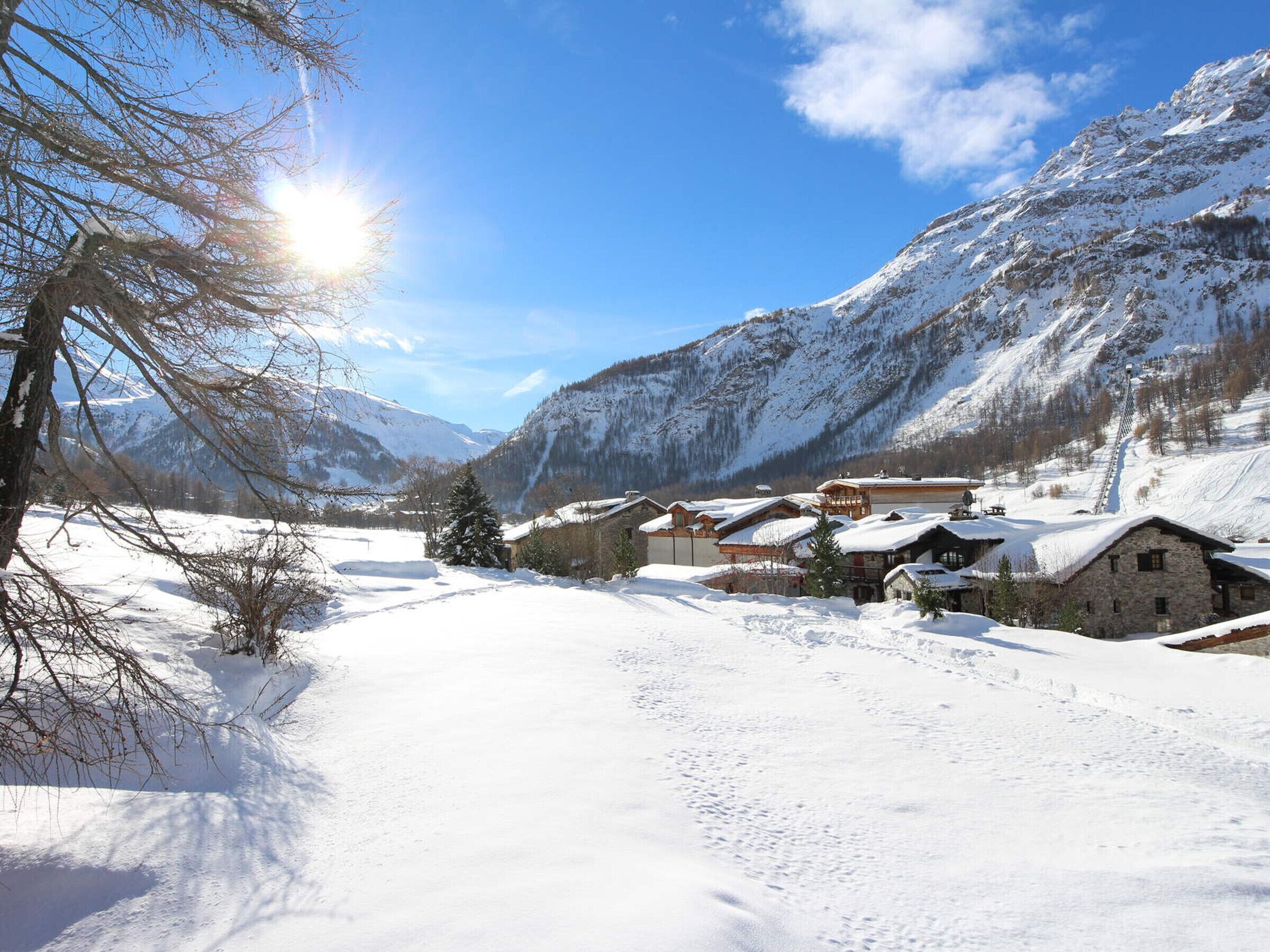 A snow-covered village with traditional wooden houses, a clear sky, and mountains in the background.