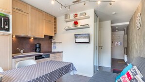 Un ambiente compatto con angolo cottura, zona pranzo con tavolo e divano con cuscino decorativo.