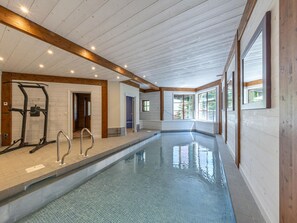 A swimming pool with a wooden deck, a gym area, and large windows.