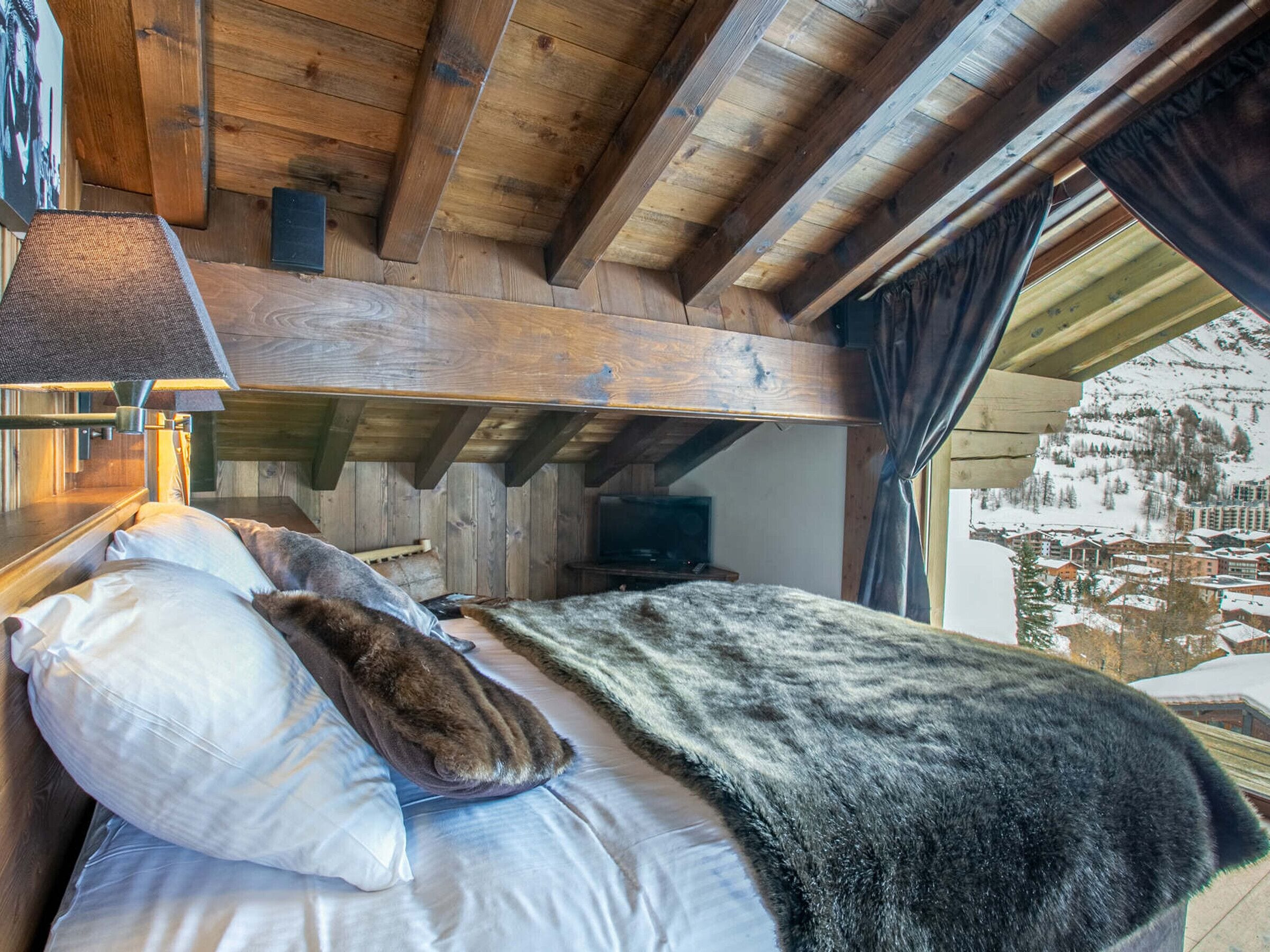 Une chambre rustique en bois, avec un lit, une lampe et une vue sur un paysage enneigé.