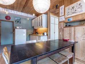 A modern kitchen with wooden cabinets, a large black table, and a white refrigerator.