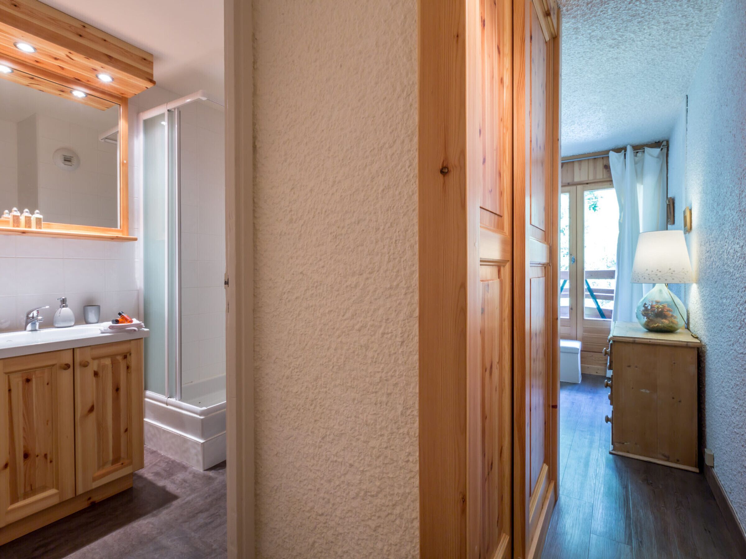 Un couloir avec une porte en bois, un meuble en bois contenant des articles de toilette et une lampe sur une table d’appoint.