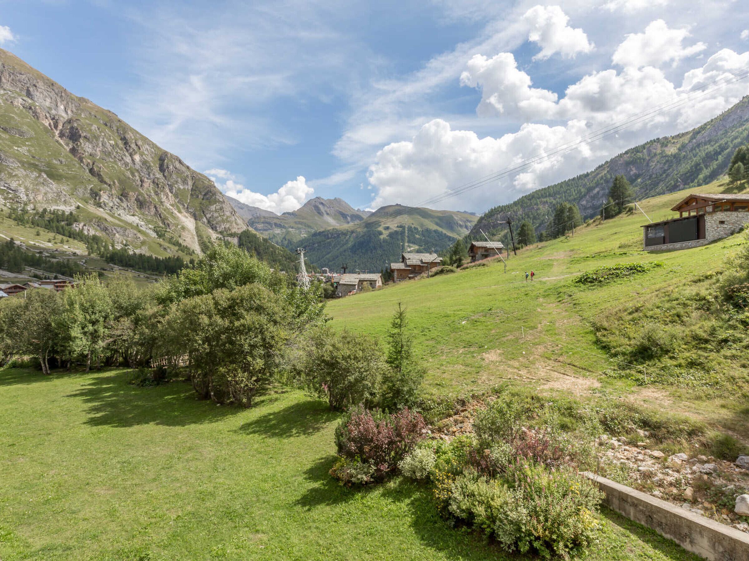 A rural village with traditional stone houses, a grassy field, and mountains in the background.