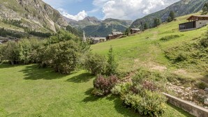 A rural village with traditional stone houses, a grassy field, and mountains in the background.