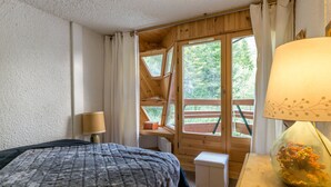 A cozy wooden cabin room with a bed, a lamp, and a view of the outdoors.
