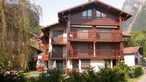 A multi-story wooden chalet with balconies, set against a mountainous backdrop. - T2 apartment with mezzanine in village center, pets allowed (Samoëns)