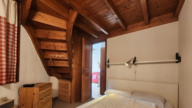 A bedroom with a wooden ceiling, a bed with white bedding, a wooden dresser, and a radiator. - T2 apartment with mezzanine in village center, pets allowed (Samoëns)