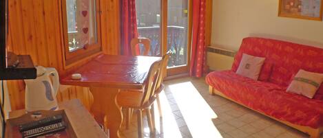 A wooden interior with a dining table, chairs, a sofa, and a window with curtains.