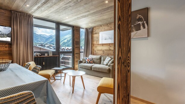 A cozy living room with a wooden ceiling, a sofa, a table, and a view of mountains through large windows. - Stunning 2-Bedroom Condo with Wi-Fi, 2 Baths & Mountain Views in Central Val-d'Isère (Val-d'Isère)
