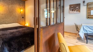 A room with a bed, a wooden-framed sliding door, a dining table with chairs, and a wall-mounted light fixture. - Stunning 2-Bedroom Condo with Wi-Fi, 2 Baths & Mountain Views in Central Val-d'Isère (Val-d'Isère)