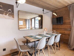A dining area with a wooden table set for four, surrounded by striped chairs, a large mirror, and a flat-screen TV mounted on the wall.
