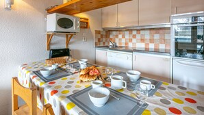 Une cuisine compacte avec une table à manger pour deux personnes, agrémentée d’une nappe à pois, d’un panier et d’un croissant.