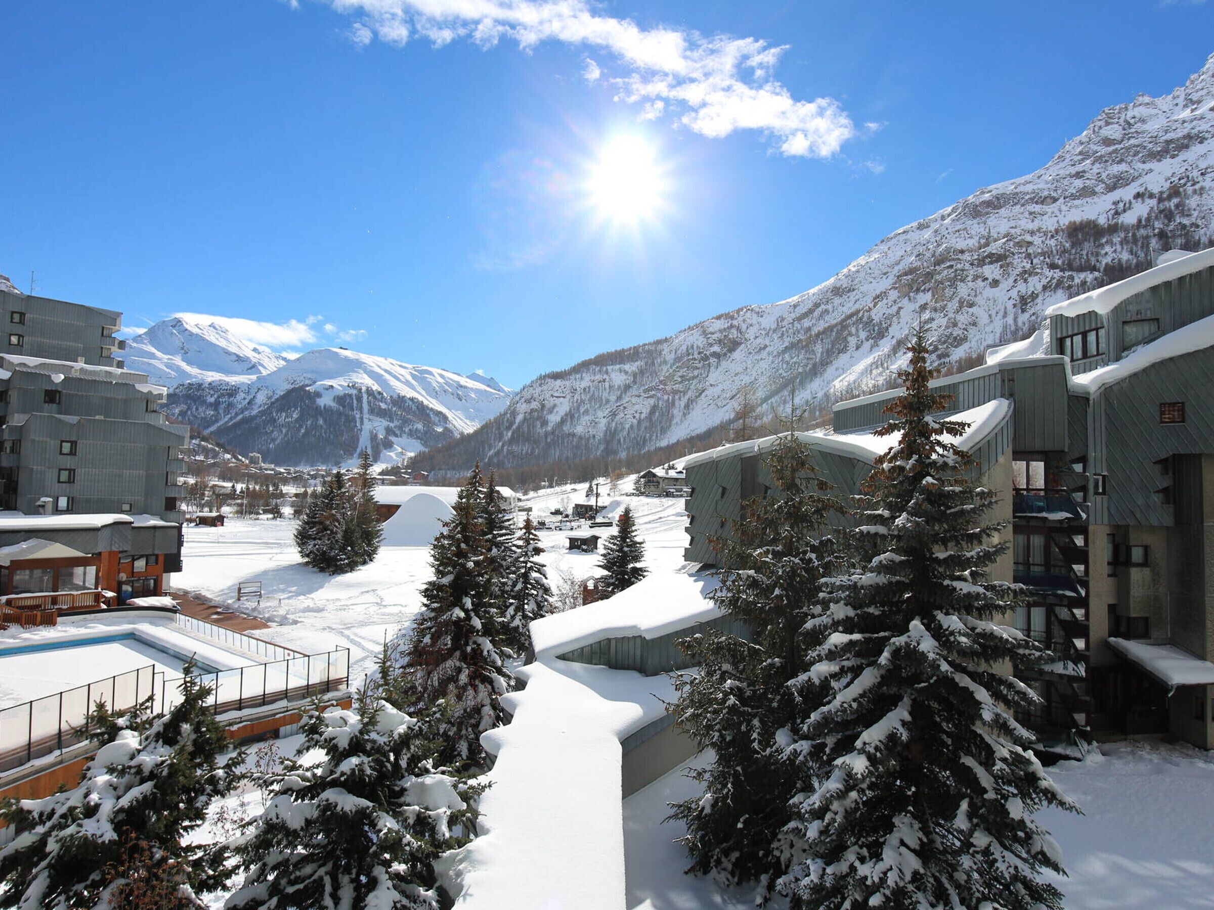 A snow-covered mountain resort with modern buildings, a ski slope, and snow-laden trees.