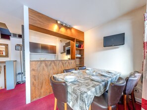 A dining area with a table set for six, wooden paneling, a TV on the wall, and a red carpet. - Comfortable triplex for 6, parking & WiFi, close to slopes (Val-d'Isère)