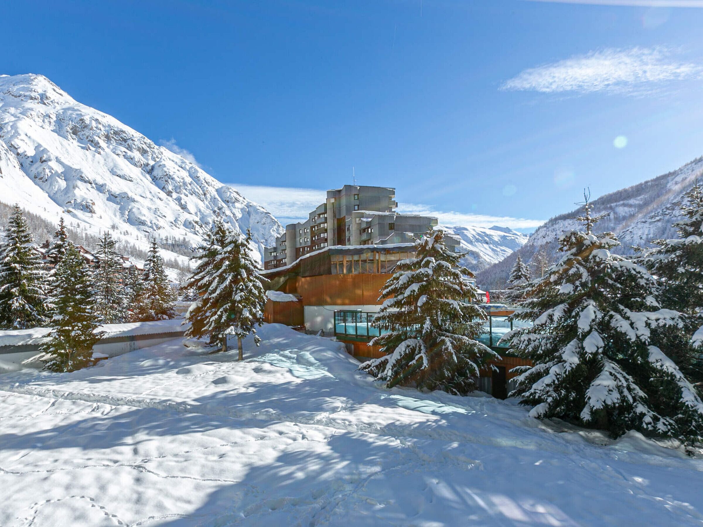 A snow-covered mountain landscape with a modern building featuring multiple floors and large windows, surrounded by snow-laden trees.
