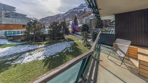 Ein Balkon mit Blick auf eine verschneite Landschaft, einen Berg und moderne Gebäude.