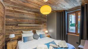 A wooden-paneled bedroom with a bed, bedside lamps, and a view through a window.