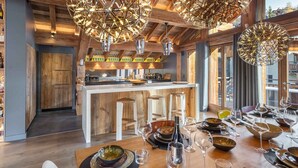 A modern kitchen with wooden beams, a central island, bar stools, and a dining area set for a meal.