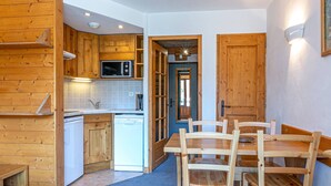 Une cuisine compacte dotée de meubles en bois, d’un four à micro-ondes et d’un lave-vaisselle. Un coin repas est aménagé avec une table et des chaises en bois.