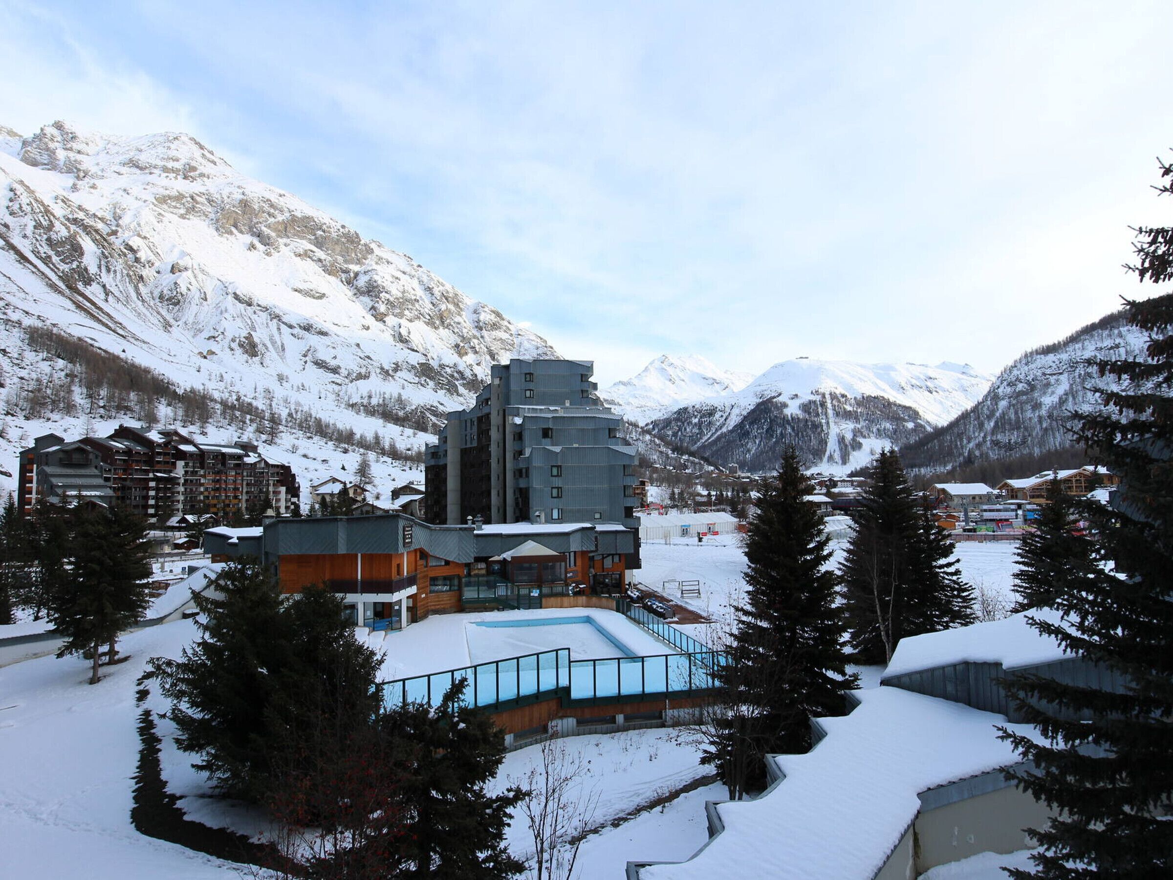 A hotel with a pool, surrounded by snow-covered mountains and trees.