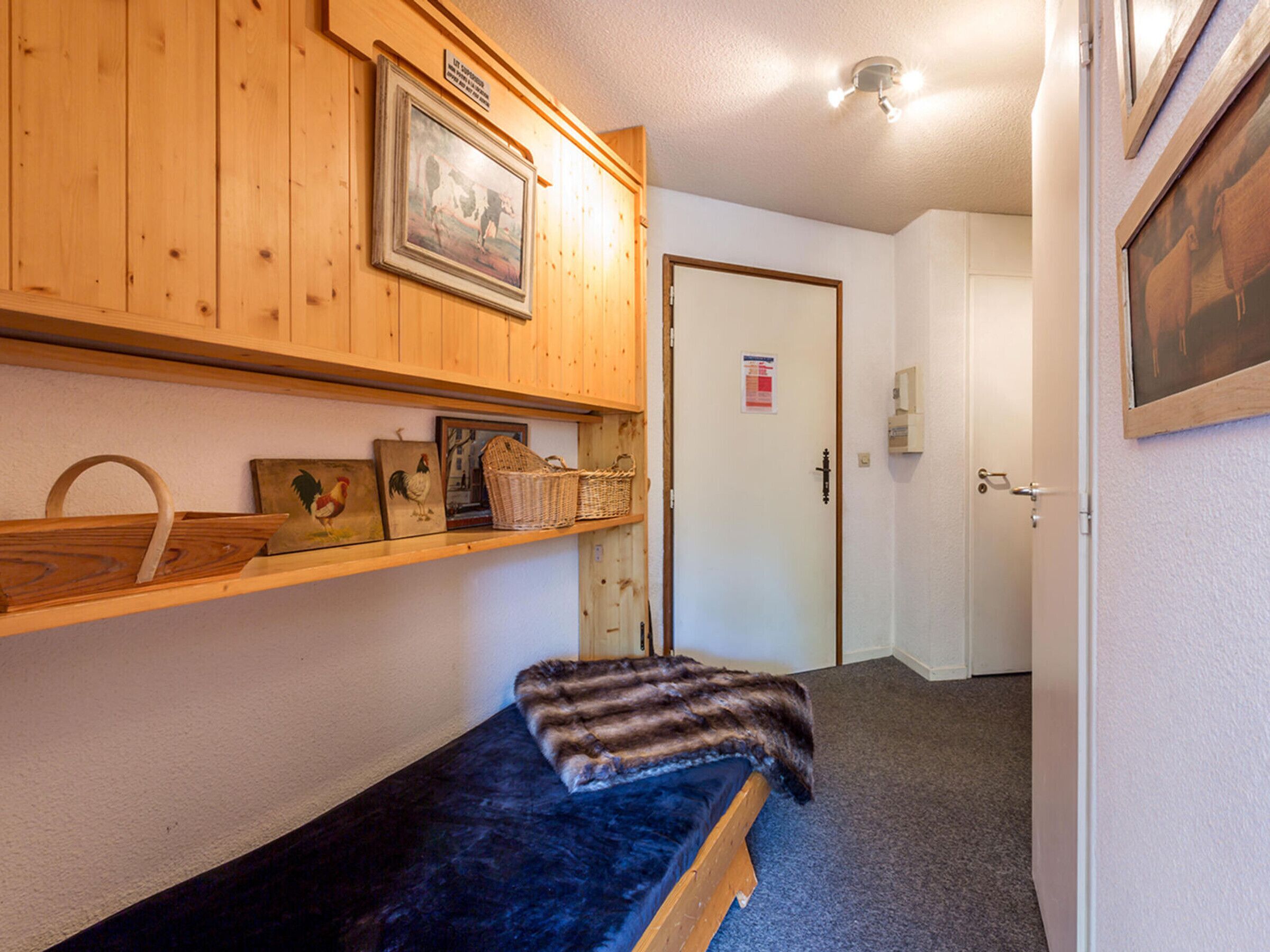 A small room with a single bed, wooden shelves with various items, a door with a sign, and a light fixture.