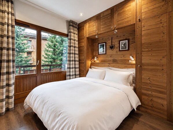 A bedroom with a wooden paneled wall, a bed with white linens, and a window with curtains.