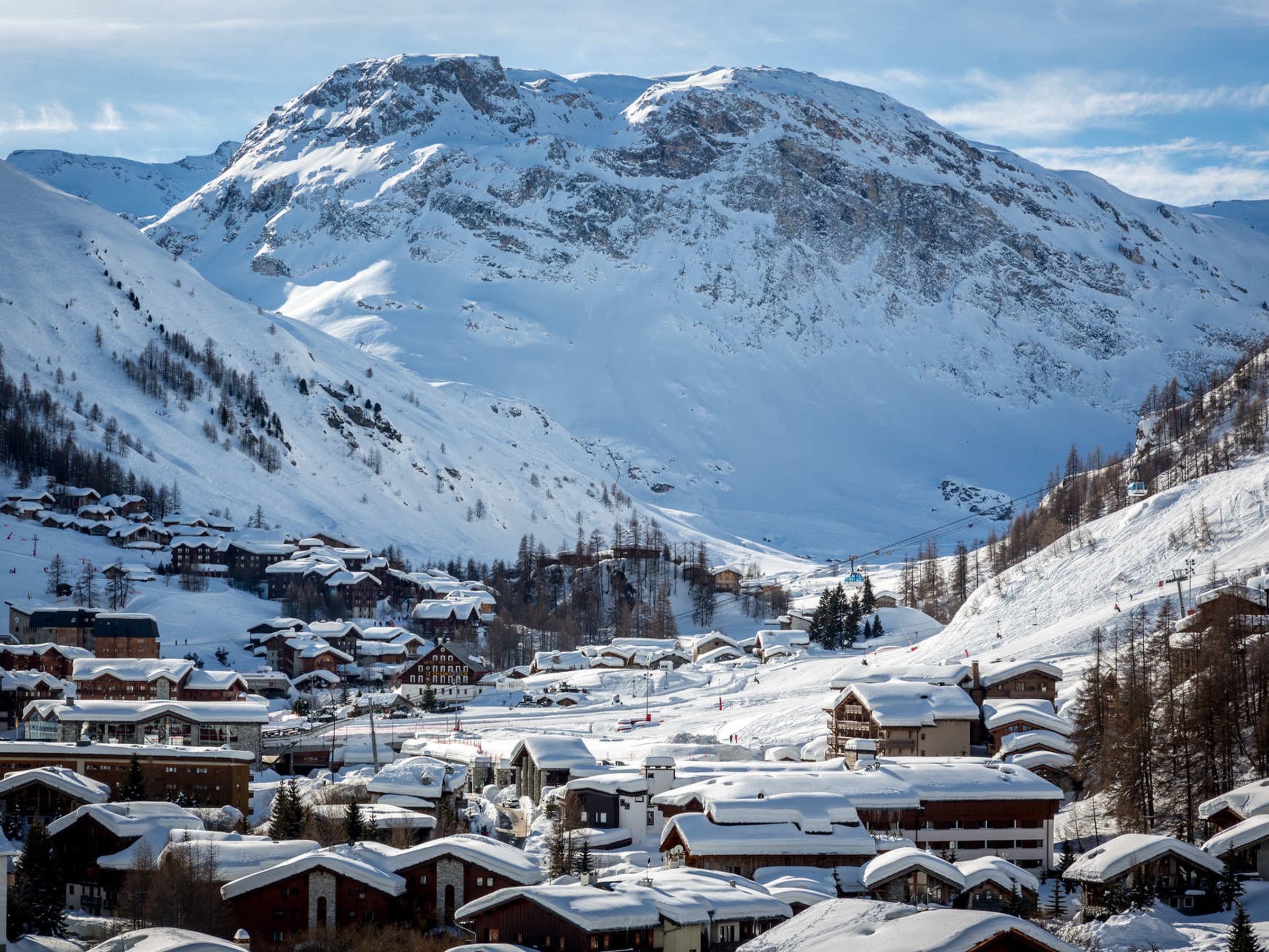 A snow-covered mountain town with traditional wooden buildings, a ski lift, and a clear view of the mountain.