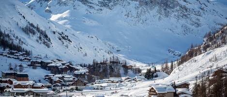 A snow-covered mountain town with traditional wooden buildings, a ski lift, and a clear view of the mountain.