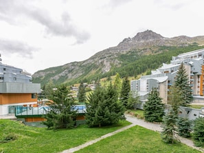 A modern hotel complex with multiple buildings, a central courtyard with trees, and a mountain backdrop.