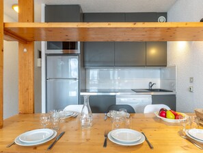 A modern kitchen with a built-in refrigerator, a dishwasher, and a sink. There is a wooden dining table set with plates, cutlery, and glasses.