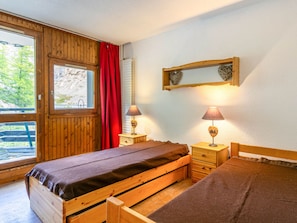 A wooden room with a bed, two nightstands, a window with a view, and a wall-mounted shelf.