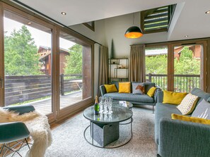 Una sala de estar moderna con sofá, mesa de centro y ventanas amplias que ofrecen vista a una terraza de madera y árboles.
