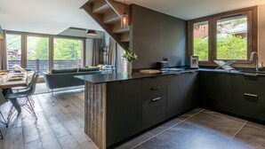 A modern kitchen with a central island, dark cabinetry, and large windows offering a view of greenery. - Elegant Duplex Apartment with Great Light, WiFi, and Parking in Val-d'Isère (Val-d'Isère)