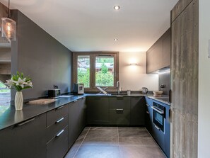 Una cocina moderna con armarios oscuros, un lavamanos de acero inoxidable y un ventanal con vistas al exterior.