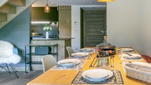 A modern dining area with a wooden table set for four, a kitchen in the background, and a staircase leading to another level. - Elegant Duplex Apartment with Great Light, WiFi, and Parking in Val-d'Isère (Val-d'Isère)