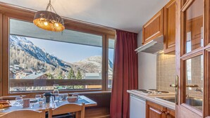 Een keuken met houten kasten, een eettafel met stoelen, uitzicht op bergen en een raam met uitzicht op een dorp.