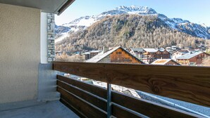 Een balkon met houten hekwerk met uitzicht op een bergdorpsplaats met traditionele houten huizen en een besneeuwde bergtop op de achtergrond.