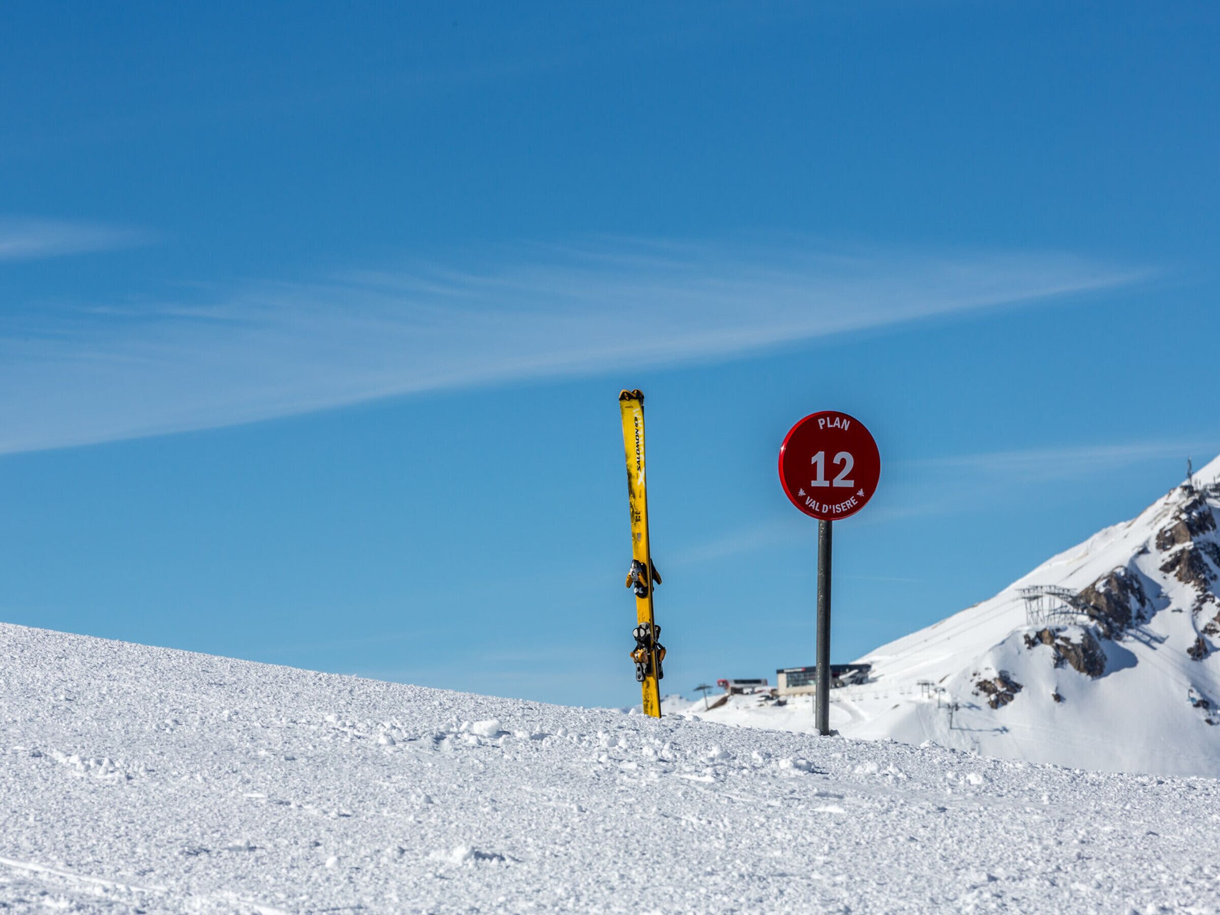 A snow-covered mountain slope with a ski lift and a red sign indicating a ski run.