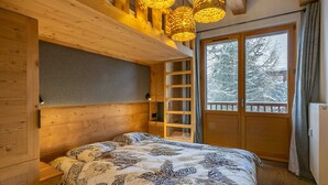 Een slaapkamer in een houten chalet met een bed, een plank en een raam met uitzicht op besneeuwde bomen.