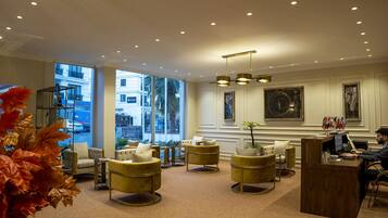 A hotel lobby with large windows, a reception desk, and several seating areas.