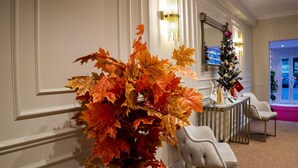 A hallway with a decorative arrangement of autumn leaves, a Christmas tree, and a seating area with a chair. - MY PALACE TUZLA (Tuzla)